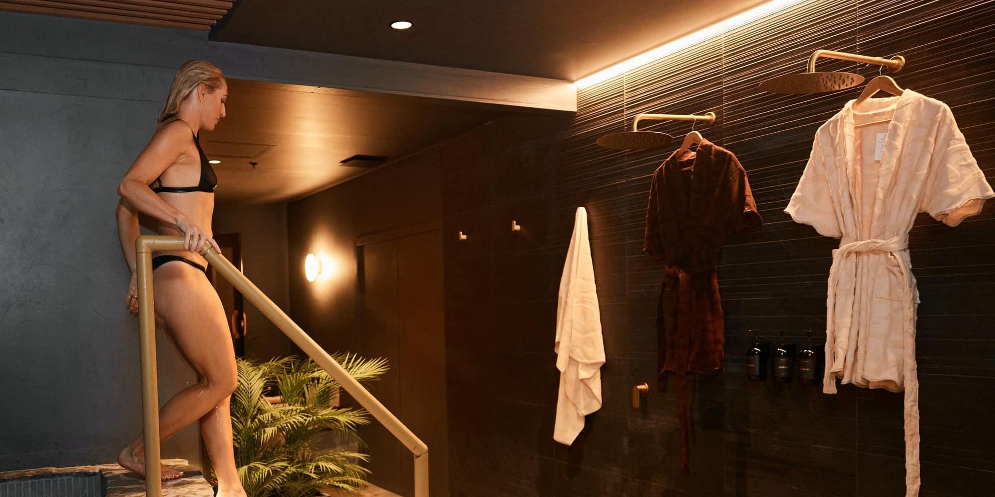 A bathhouse plunge pool with stone steps and robes hanging on the wall beyond.